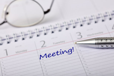 A detailed calendar page with a handwritten meeting reminder, complemented by a pen and glasses.の写真素材