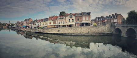 Wide-angle view showcasing picturesque riverbank architecture, a charming stone bridge, and calm waters.の写真素材
