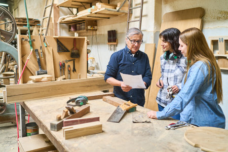 An experienced worker guides two younger colleagues in a lumberyard, showing teamwork and mentorship in woodworking. Tools and wood materials are visible, highlighting a practical work environment.の写真素材