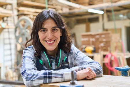 A confident young woman smiles while working in a busy lumberyard, showing her skills and dedication. The dynamic environment highlights teamwork and craftsmanship in the woodworking industry.の写真素材