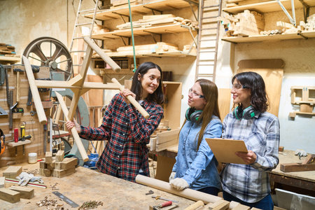 A team of women engaged in woodworking, showcasing training and collaboration in a lumberyard. The group is focused on creating a project together, demonstrating teamwork and skill development.の写真素材