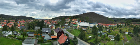 Wide panoramic view of a countryside village with colorful houses, lush greenery, and cloudy skies....