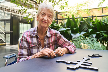 Elderly lady engaged in a crossword-style board game outside in a retirement facility garden,...