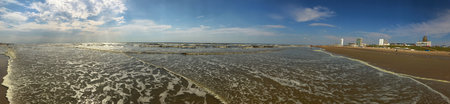 An expansive panoramic image showing a scenic beach, with city buildings and a blue sky.