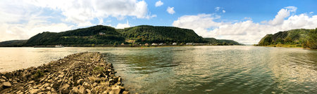 A stunning panorama of a picturesque river surrounded by verdant hills under a partly cloudy sky. Ideal for representing nature's beauty, harmony, and the tranquility of serene water and landscapes.の写真素材