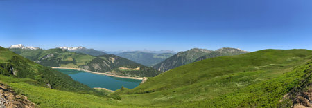 Expansive panoramic landscape showcasing a verdant valley, a tranquil lake, and distant mountain ranges under a bright clear sky. Perfect for nature, outdoor, travel, or scenic photography headers.の写真素材