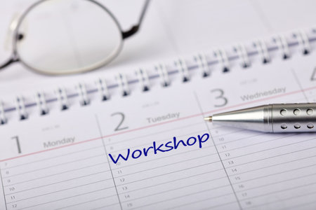 Calendar page with the word 'workshop' handwritten, accompanied by a pen and glasses, symbolizing organization, planning, and preparation for upcoming events. Ideal for scheduling or time management themes.の写真素材