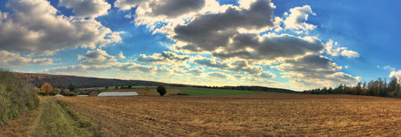 A tranquil rural landscape showcasing an open field with dynamic cloud formations above.の写真素材