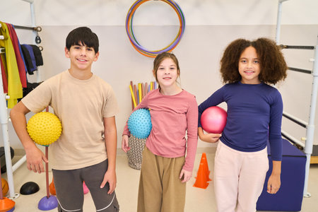 Three kids participate in a pediatric physiotherapy session at a rehab center, using therapy balls and balance equipment to improve motor skills and coordination in a friendly, supportive group environment.の写真素材