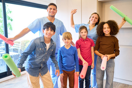A cheerful group of kids with two therapists in blue scrubs engage in a playful therapeutic exercise, promoting balance, mobility, and motor skills in a pediatric rehab setting.の写真素材