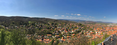 A wide panoramic view of a picturesque town surrounded by verdant hills beneath a vibrant blue sky, highlighting the beauty of tranquil landscapes and serene communities.の写真素材