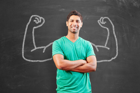Young man as a proud student or young teacher in front of a blackboard with muscular arms,...