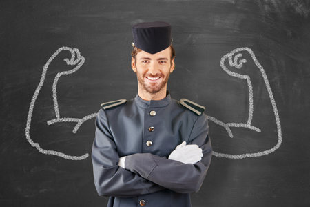 Friendly page in uniform in front of a blackboard with muscular arms, representing the concept of service.の写真素材