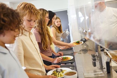 Students waiting in line at a cafeteria serving counter to receive their meals.の写真素材