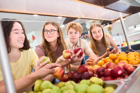 A group of students choose fresh fruits at a school cafeteria, promoting healthy eating.の写真素材
