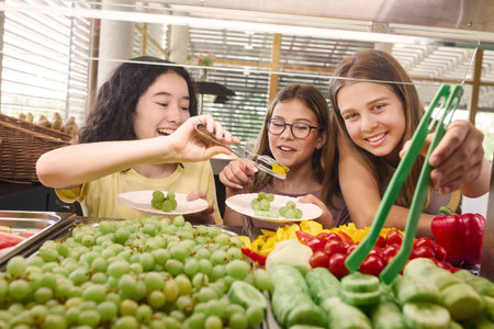 Three children enjoying picking healthy food options like fruits and vegetables from a school cafeteria. A cheerful, healthy eating environment promotes wellness and encourages positive eating habits in young students.の写真素材