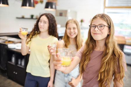 Three young students cheerfully enjoying drinks in a clean and modern school cafeteria environment.の写真素材