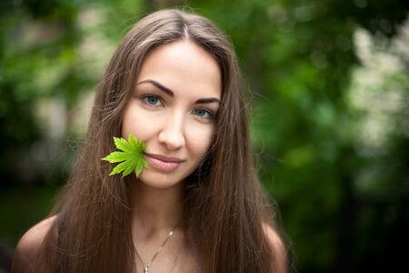 Beautiful girl with a maple leaf in her mouth. Green leaves  background. Nature.の写真素材