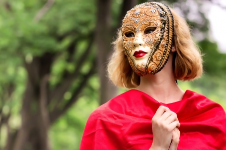 Blond woman in carnival mask over foliage backgroundの写真素材
