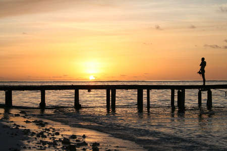 Man standing on jetty at maldive island in front of sunsetの写真素材