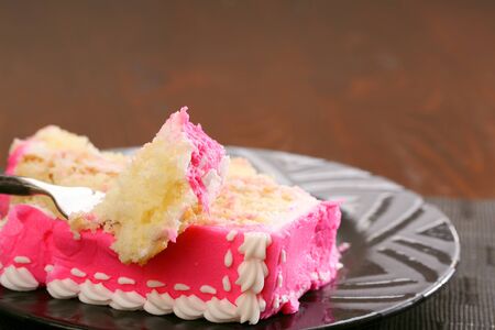 Piece of butter creme yellow cake with pink frosting on a forkの写真素材