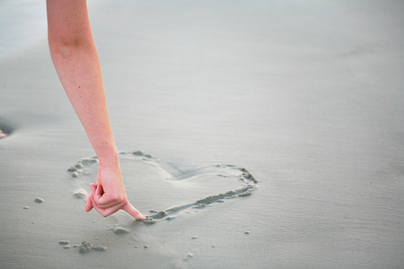 Love message of a drawn heart in sand at water's edgeの写真素材