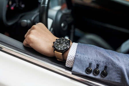 Close up of a man's hand holding a wristwatch while driving a car