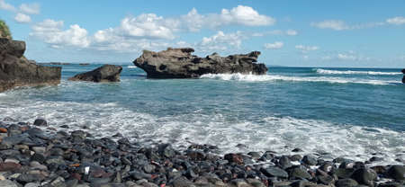 Black stones on the beach add to the beauty of the amazing natural scenery with blue skies on sunny daysの写真素材