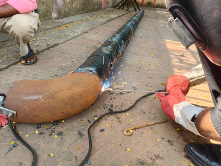 A man is welding a thick iron pipe. The worker is welding a patch onto a large, dark colored pipe....