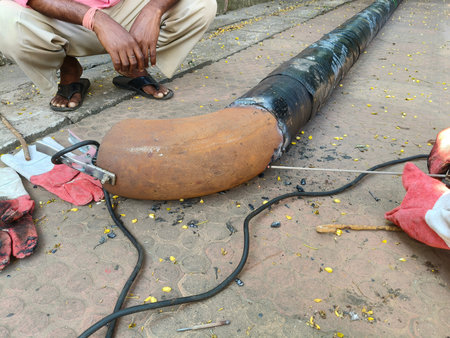 A man is welding a thick iron pipe. The worker is welding a patch onto a large, dark colored pipe....