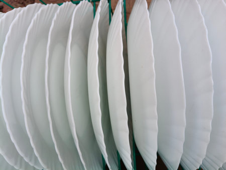 A teal wire basket filled with several white, scalloped-edge plates. Arranged neatly in lines. This...