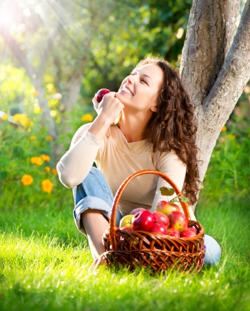 Happy Smiling Young Woman Eating Organic Apple in the Orchard の写真素材