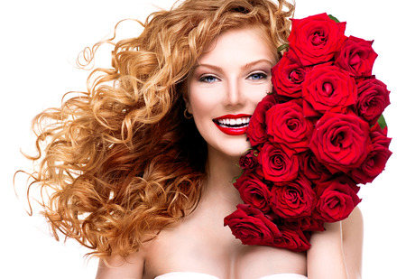 Beauty woman with long permed red hair and beautiful red rosesの写真素材