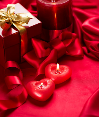 Valentines Day. Red heart shaped candles and gift on red silkの写真素材
