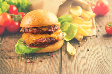 Fresh homemade burger with meat patties served with ketchup sauce with grilled potatoes on wooden table. Cheeseburger close up. Burger with vegetables and French Fries. Vintage rustic styleの写真素材