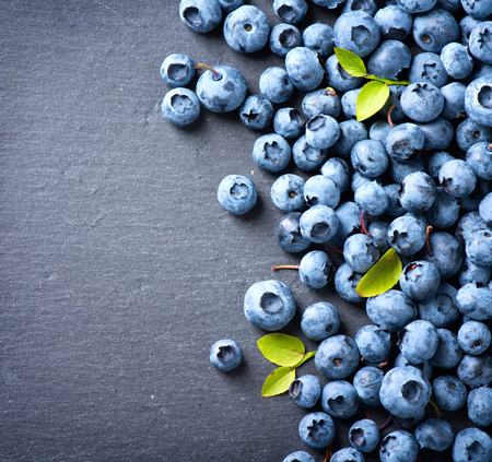 Blueberry border design. Ripe and tasty blueberries with green leaves on dark background. Bilberries close-up. Copy space for your text. Healthy food conceptの写真素材