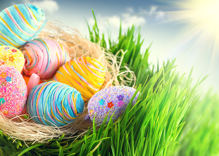 Easter colorful eggs in the nest on spring green grass over blue skyの写真素材