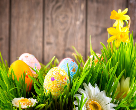 Easter border design. Colorful eggs in spring grass meadow over wooden backgroundの写真素材