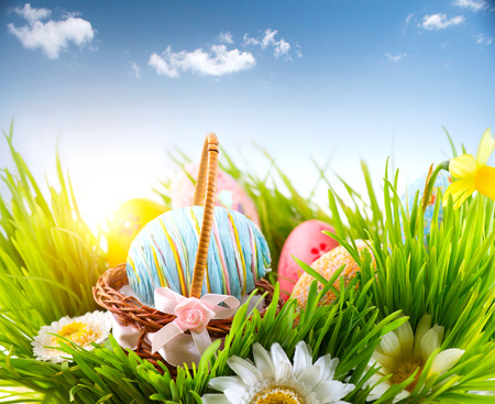 Easter. Colorful eggs in spring grass meadow over blue skyの写真素材