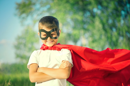 Little boy wearing superhero costume and having fun outdoorsの写真素材