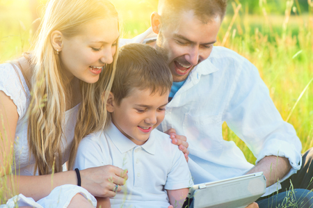 Happy young family with kid using tablet pc in summer parkの写真素材