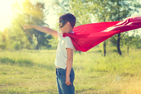Little boy wearing superhero costume and having fun outdoorsの写真素材