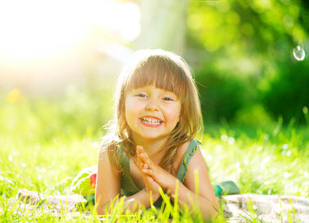 Portrait of a smiling little girl lying on green grassの写真素材