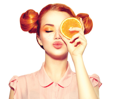 Beautiful joyful teen girl with freckles holding juicy orange sliceの写真素材