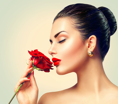 Fashion brunette model girl face portrait with red rose in her handの写真素材