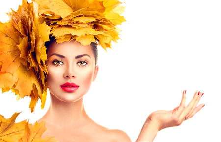 Fall. Beauty model girl with autumn bright leaves hairstyle. Girl showing empty copy space on open hand palmの写真素材