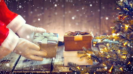 Santa Claus putting gift box under the Christmas tree with blinking garlandsの写真素材