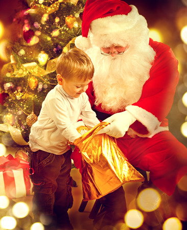Christmas holiday scene. Cute little boy and Santa Claus holding giftboxの写真素材