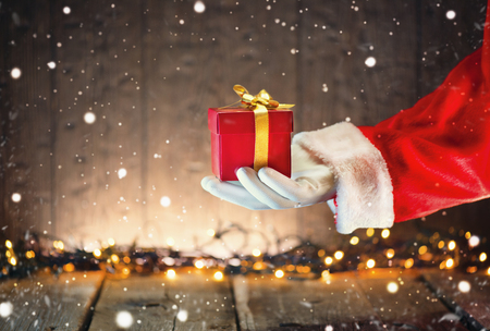 Santa Claus holding Christmas gift box over wooden backgroundの写真素材