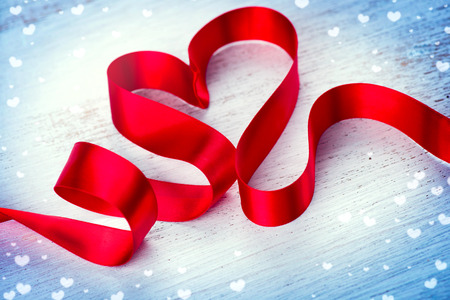 Valentine's day. Red heart shaped satin ribbon over white wooden backgroundの写真素材